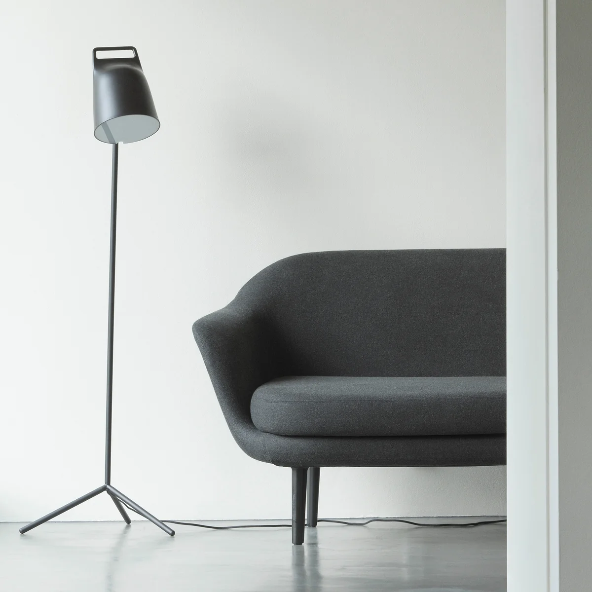 De Stage LED-vloerlamp van Normann Copenhagen naast een grijze bank.