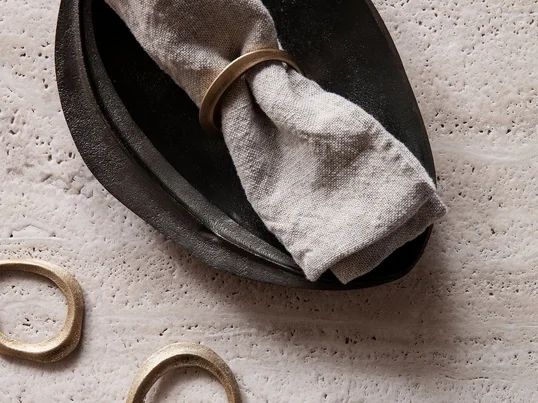 Lifestyle productafbeelding van de decoratieve Flow servetringen van messing in een praktische set van 4 en de Forest decoratieve schaal van messing in zwart van Ferm Living.