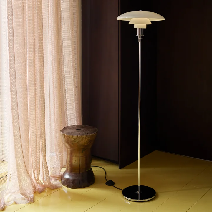De PH vloerlamp, hoogglans verchroomd van Louis Poulsen in een verduisterde slaapkamer.