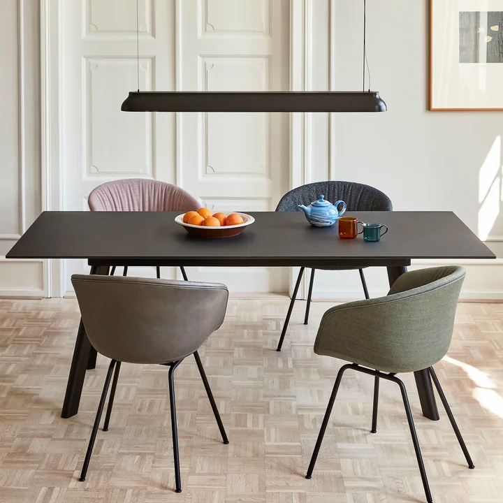 De PC Lineaire staaf hanglamp, zacht zwart van HAY boven een zwarte rechthoekige eettafel