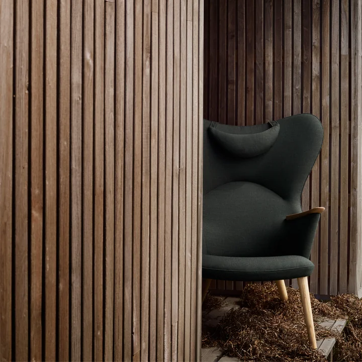 De CH78 Mama Bear Lounge Chair van Carl Hansen tussen rustieke houten muren