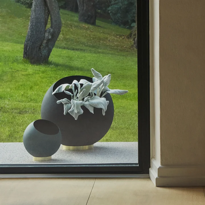 De Globe bloempot van AYTM in zijn verschillende maten achter een kamerbreed raam buiten