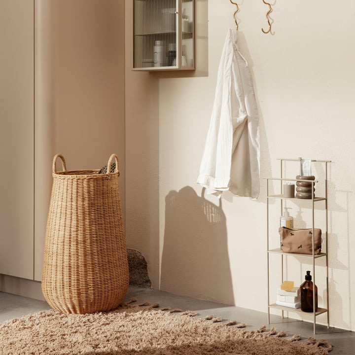 De Braided rotan wasmand door te fermenteren Leven op een beige tapijt naast een kleine plank met badkameraccessoires