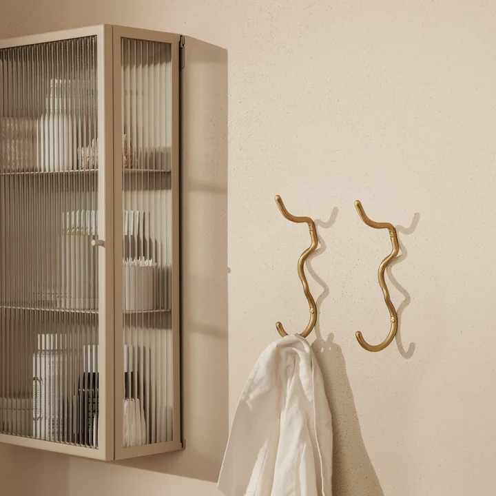 De Curvature wandhaak van Ferm Living met een handdoek naast een wandvitrine