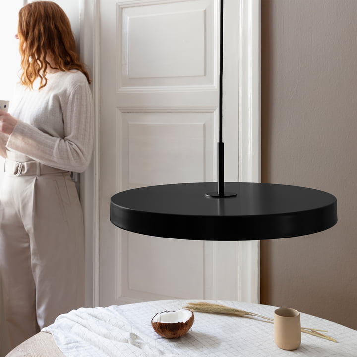 De Asteria LED hanglamp van Umage in zwart / zwart boven een ronde, witte eettafel