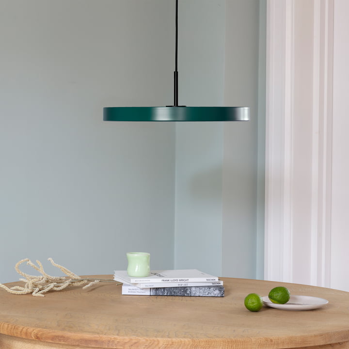 De Asteria LED hanglamp van Umage in zwart / forest green boven een lichtkleurige, ronde houten eettafel