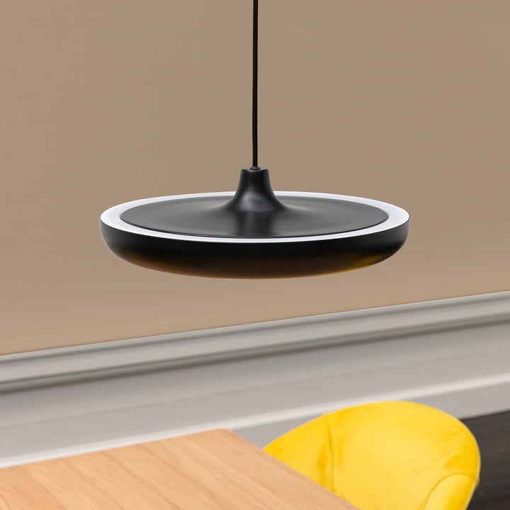 De pendelarmatuur Cassini Medium LED van Umage in zwart boven een houten tafel met gele stoel