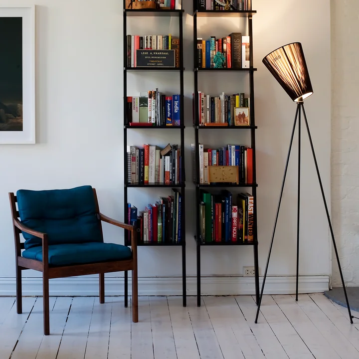 De Oslo Wood vloerlamp van Northern naast de boekenkast en een benzineblauwe fauteuil.