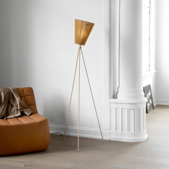De Oslo Wood vloerlamp van Northern naast een bruine leren fauteuil en een witte muur.