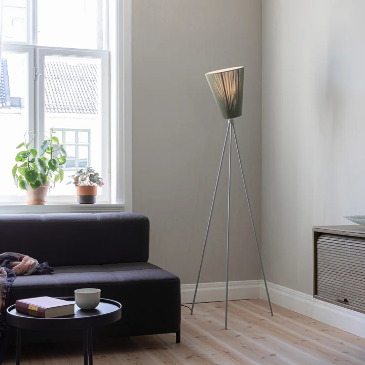 De Oslo Wood vloerlamp van Northern in het woongedeelte naast een donkere bank.