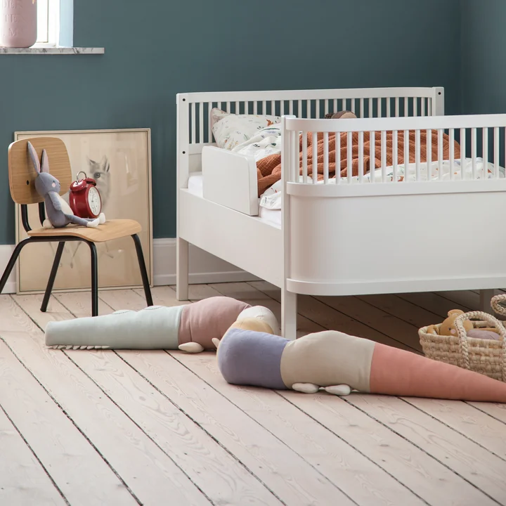 Het speelse Sleepy Croc kussen van Sebra naast het witte kinderbed