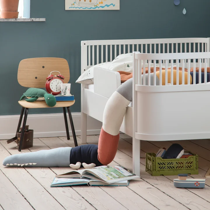 Het Sleepy Croc kussen en de Oakee stoel van Sebra naast het witte kinderbed