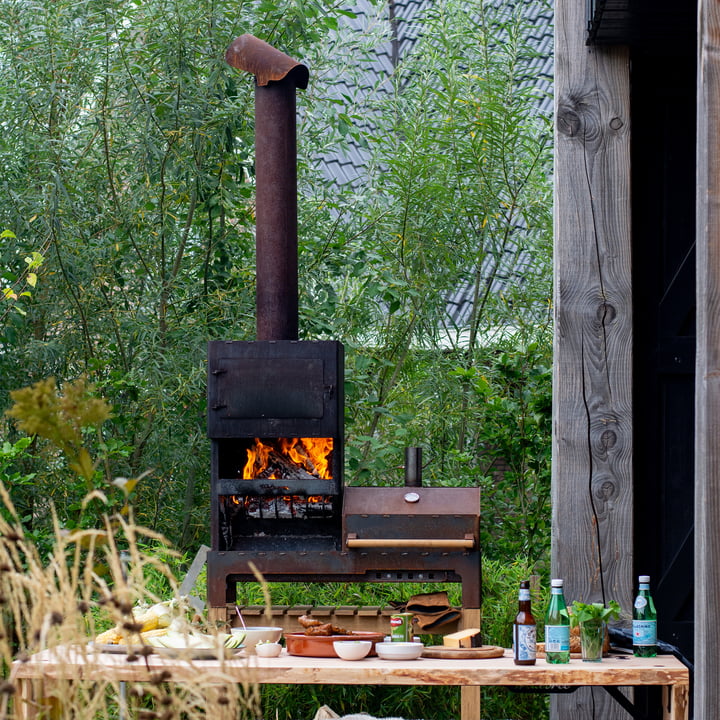 De Outdoor stalen kachel XL van Weltevree achter een eettafel in de open lucht.