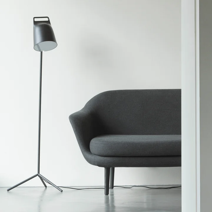 De Stage LED-vloerlamp van Normann Copenhagen naast een grijze bank.